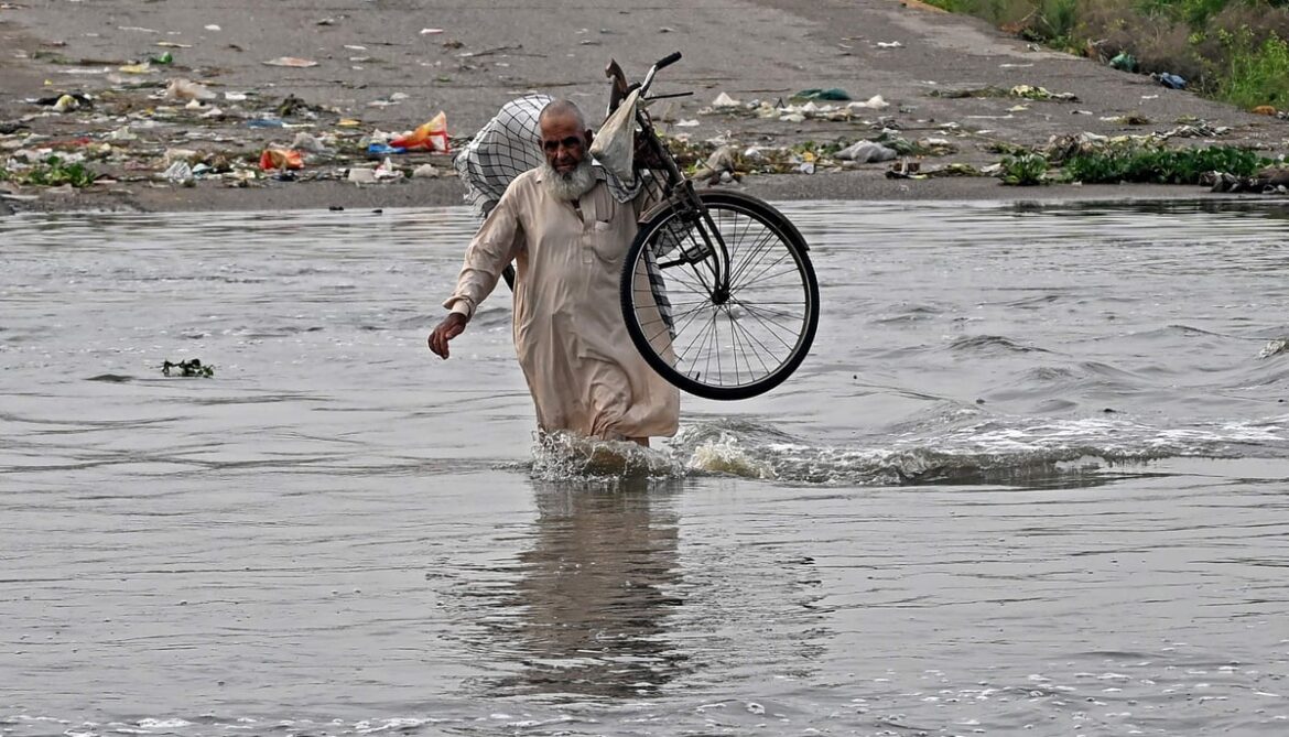 A man carries his bicycle as he wades along a flooded road after heavy monsoon rains in Karachi on August 20, 2025. — AFP