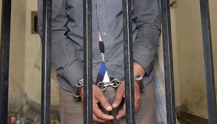 Karachi house help arrested for amassing millions in hidden assets A representational image showing a person handcuffed and standing behind bars. — AFP/File