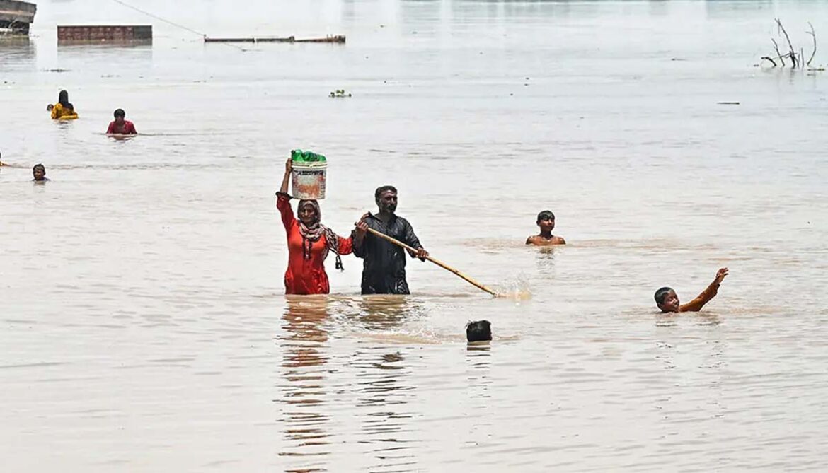 People wade through a flooded area after heavy monsoon rains induced a rise in the water level of the River Ravi in Muridke on July 27, 2026. — AFP